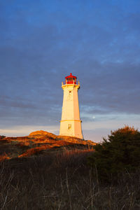 Lighthouse on field by building against sky