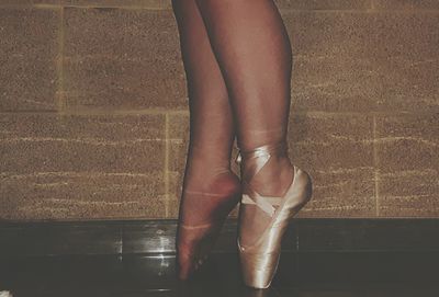 Low section of woman tiptoeing against wall
