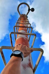 Low angle view of hand holding metal against sky