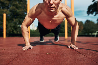 Young shirtless man bodybuilder doing push-ups on a red rubber ground during his workout