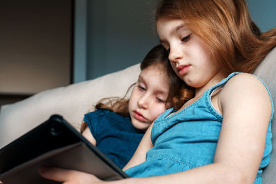 Cute sisters watching video over digital tablet on bed at home