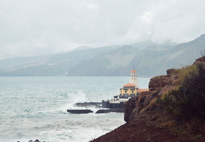 Scenic view of sea by mountain against sky