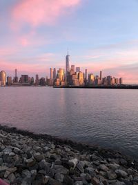 Sea by buildings against sky during sunset