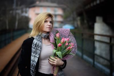 Young woman holding flower bouquet standing against wall