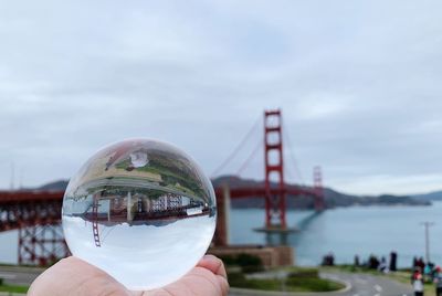 Cropped image of person holding crystal ball against sky