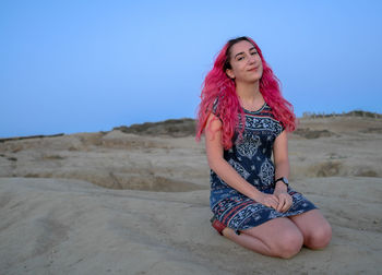 Beautiful young woman sitting on land against clear sky