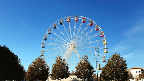 Low angle view of ferris wheel and trees against blue sky