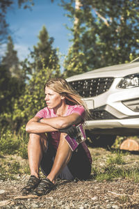 Woman in cycling clothes sitting near car