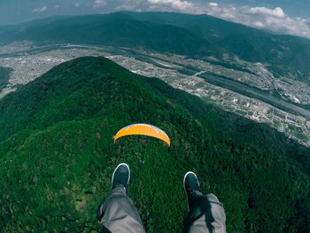 Low section of person paragliding above mountain against sky