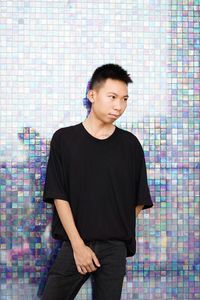 Young man looking away while standing against wall