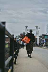 Rear view of man walking on railing in city