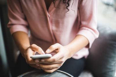 Midsection of young businesswoman text messaging from smart phone at creative office