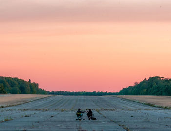 People on road against clear sky during sunset