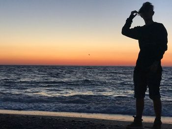 Silhouette man photographing sea against sky during sunset