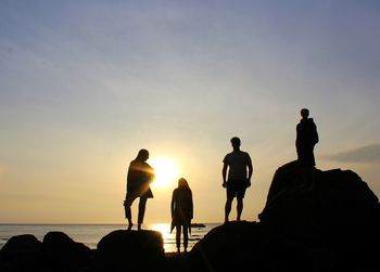 Silhouette people on rock at beach against sky during sunset