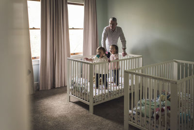 Twin toddler girls in bedroom crib as father look on