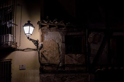 Illuminated street light by wall of building at night