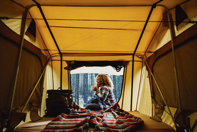 Smiling woman sitting against trees seen through tent