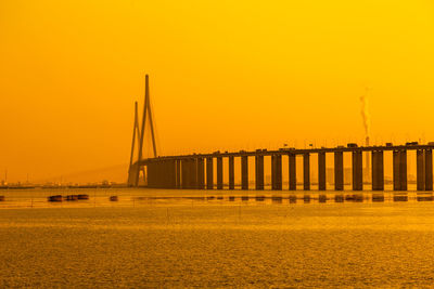 Bridge over sea against orange sky