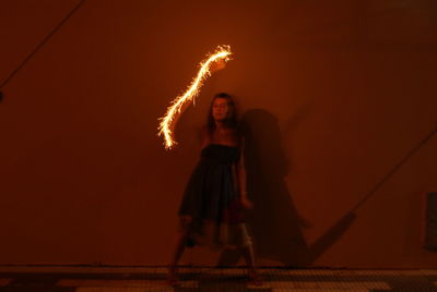 Blurred motion of woman holding illuminated sparkler against wall at night