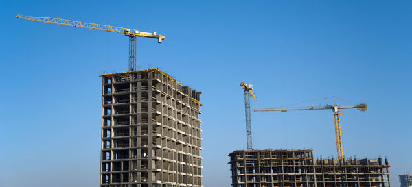 Low angle view of crane by building against clear blue sky