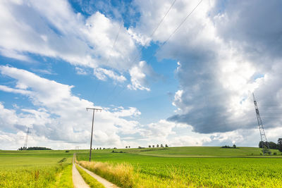 Footpath amidst grassy field against cloudy sky