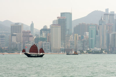 Sailboats in sea by buildings against sky in city