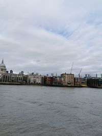 View of buildings by sea against cloudy sky