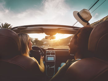 Rear view of women laughing while sitting in car against sky