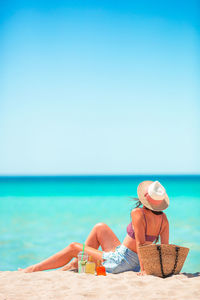 Man sitting on beach by sea against clear sky