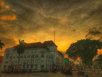 Cars on street by buildings against sky during sunset