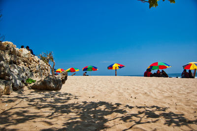 People on beach against clear blue sky