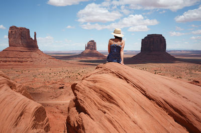Rear view of woman sitting on rock formation in desert against landscape
