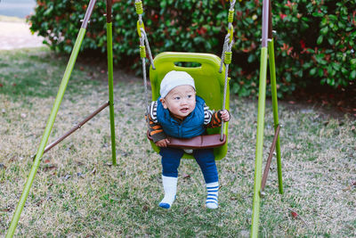 Cute baby boy sitting in swing at playground