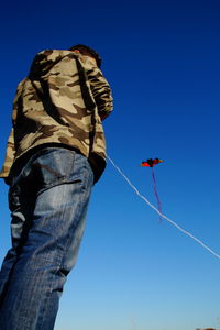 Low angle view of man flying kite against clear blue sky