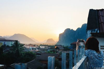 Rear view of woman photographing cityscape against sky during sunset