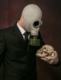 Businessman an wearing gas mask while holding skull