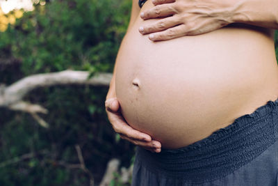 Midsection of pregnant woman with hands on stomach standing outdoors