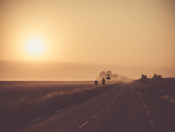 Road amidst field against sky during sunset