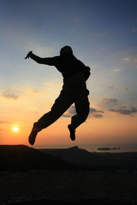 Silhouette man jumping against sky during sunset