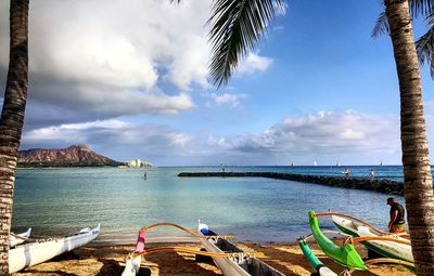 Outrigger boats at beach against cloudy sky