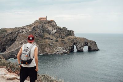 Rear view of man standing on rock by sea against sky