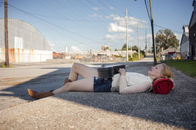 Thoughtful woman lying on sidewalk against electricity pylons