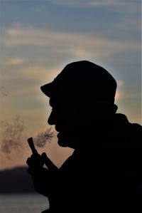 Silhouette man smoking against sky during sunset