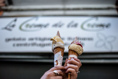 Cropped hands of woman holding ice cream cones against banner