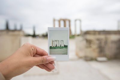 Cropped hand of woman holding photograph against old ruins