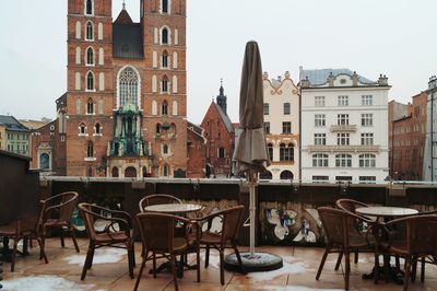 Empty chairs and tables at sidewalk cafe against buildings in city