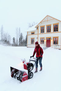 Woman using snowblower in front of house