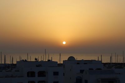 Silhouette buildings by sea against sky during sunset