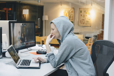 Side view of computer programmer using laptop at desk in office